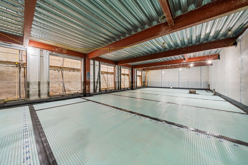 Interior construction showing steel beams and floor preparation with windows.