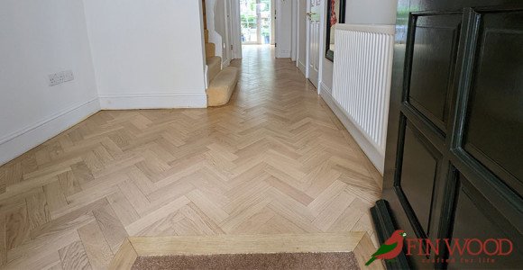 Light wood flooring in a hallway with a staircase.