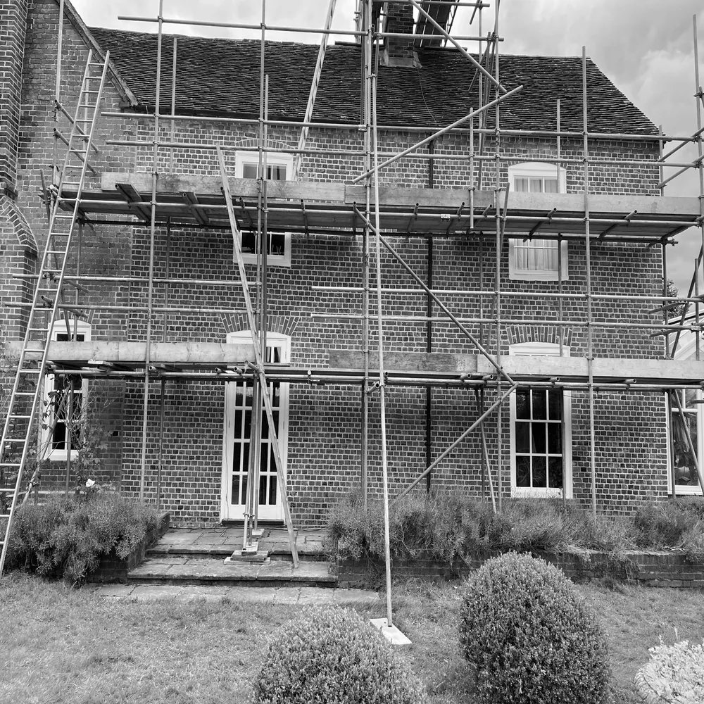 Black and white image of a brick building with scaffolding, showcasing brickwork and potential restoration work. The lack of color slightly reduces its impact.