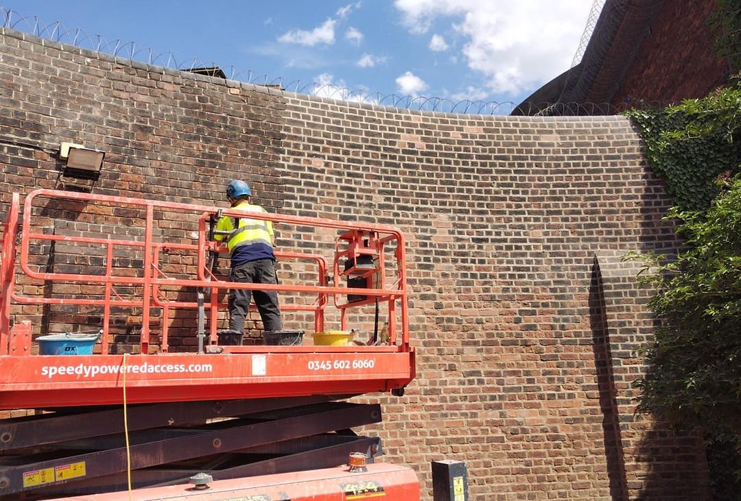 Image of a worker on a lift restoring a large brick wall.
