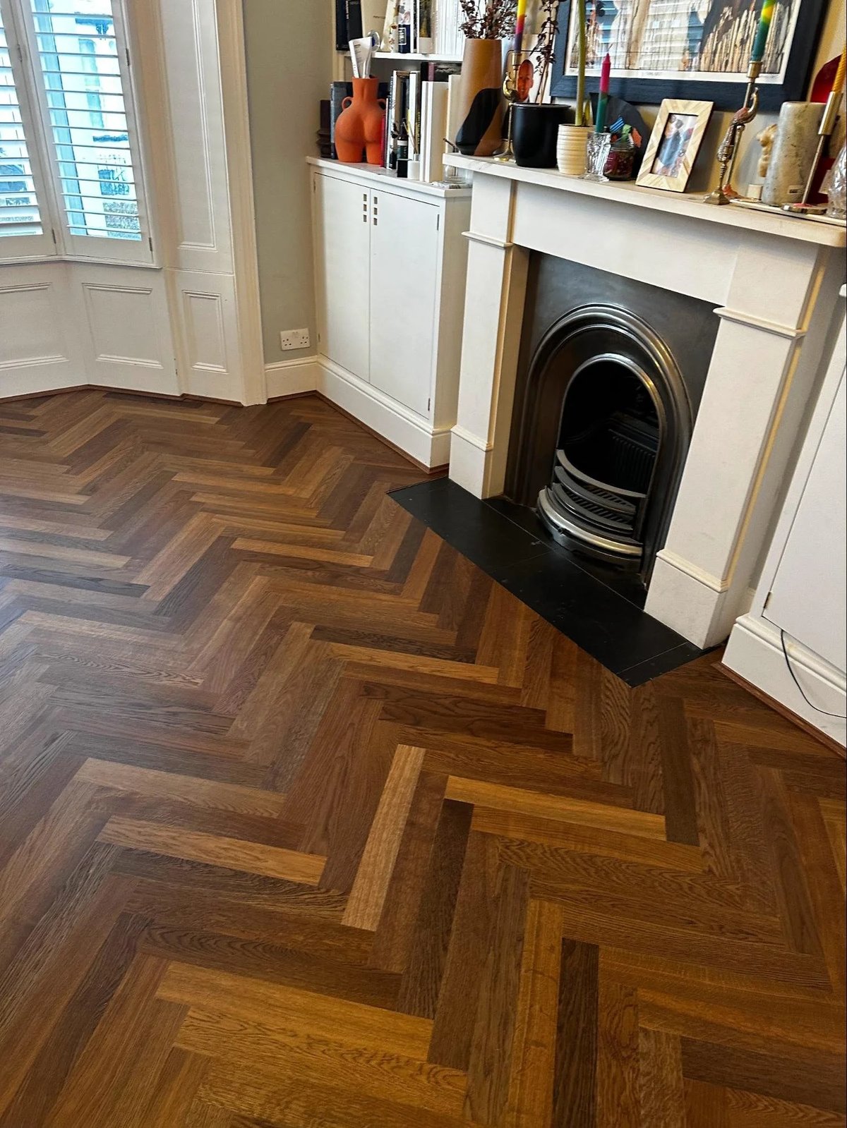 Herringbone wood floor after refinishing, near a fireplace.