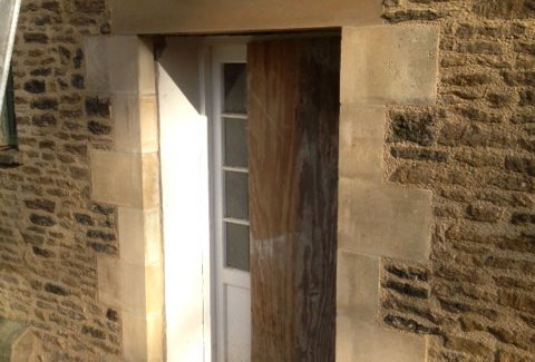 Stone wall restoration in progress around a doorway, with equipment visible.