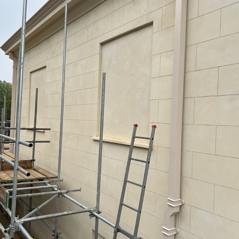 Exterior wall with lime plastering, showing scaffolding and ladder, indicating ongoing restoration work.