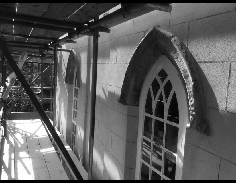 Black and white image of a building with arched windows and scaffolding, suggesting period restoration.