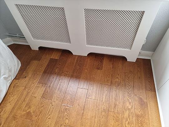 Close-up of wood flooring installed around a radiator cover, highlighting detail and precision.