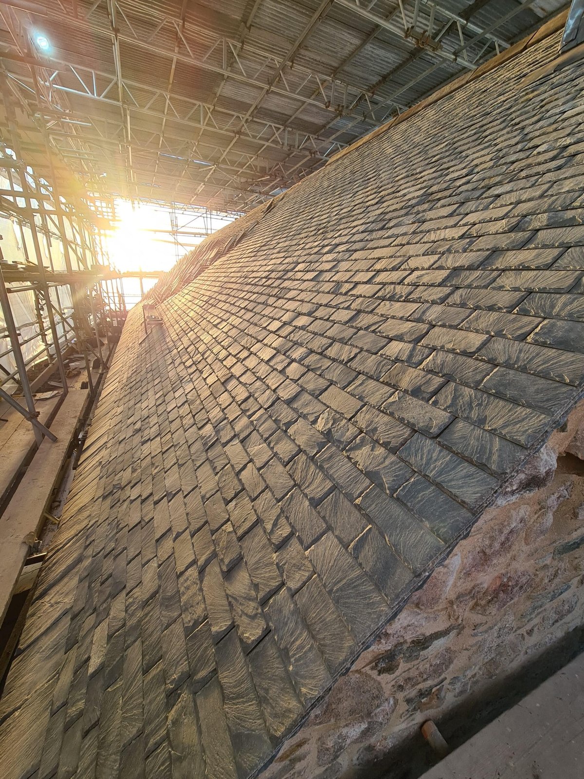 Slate roof under construction with scaffolding and sunlight.
