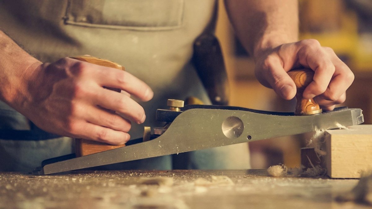 Close-up of a craftsman using a hand plane on a piece of wood, showcasing joinery skills.