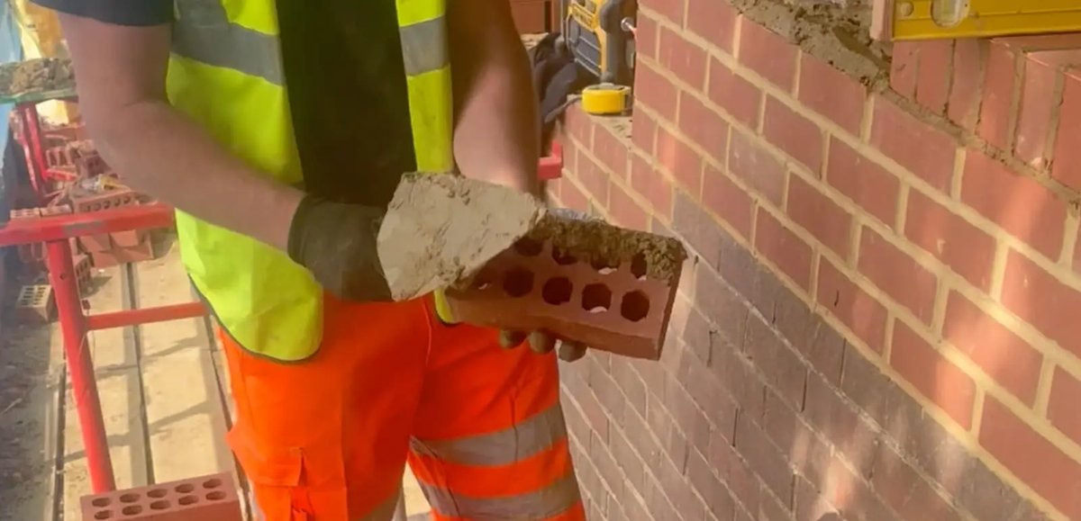 Bricklayer holding a brick with mortar, showcasing the building process.