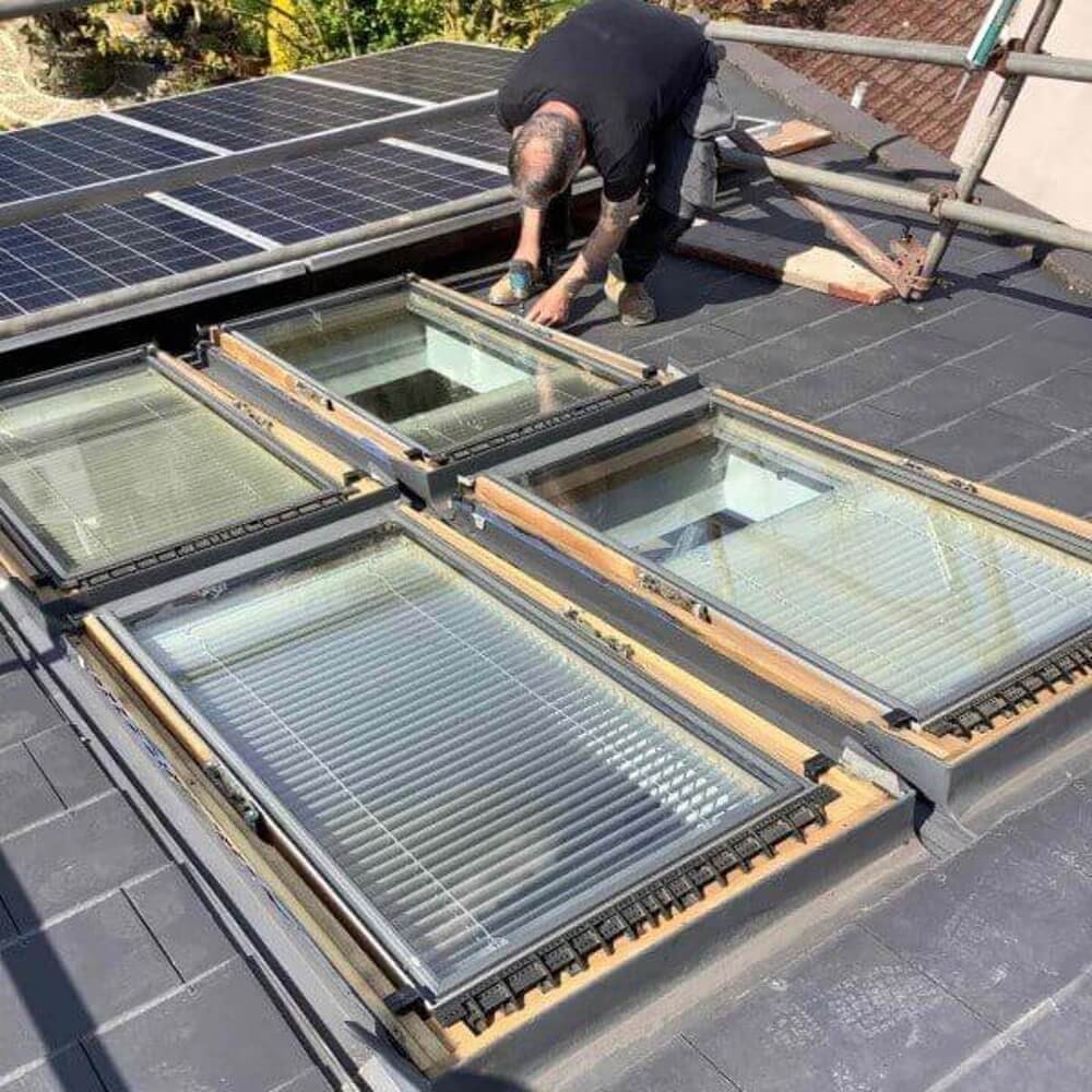 Roofer installing skylights on a slate roof with solar panels.