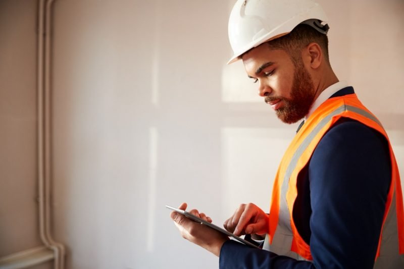 Man in hard hat and safety vest using a tablet, possibly surveying a property.