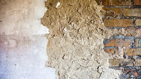 Damaged wall showing brick and plaster, indicating restoration needs.