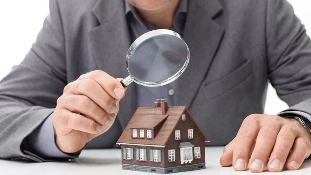 Man inspecting a model house with a magnifying glass.