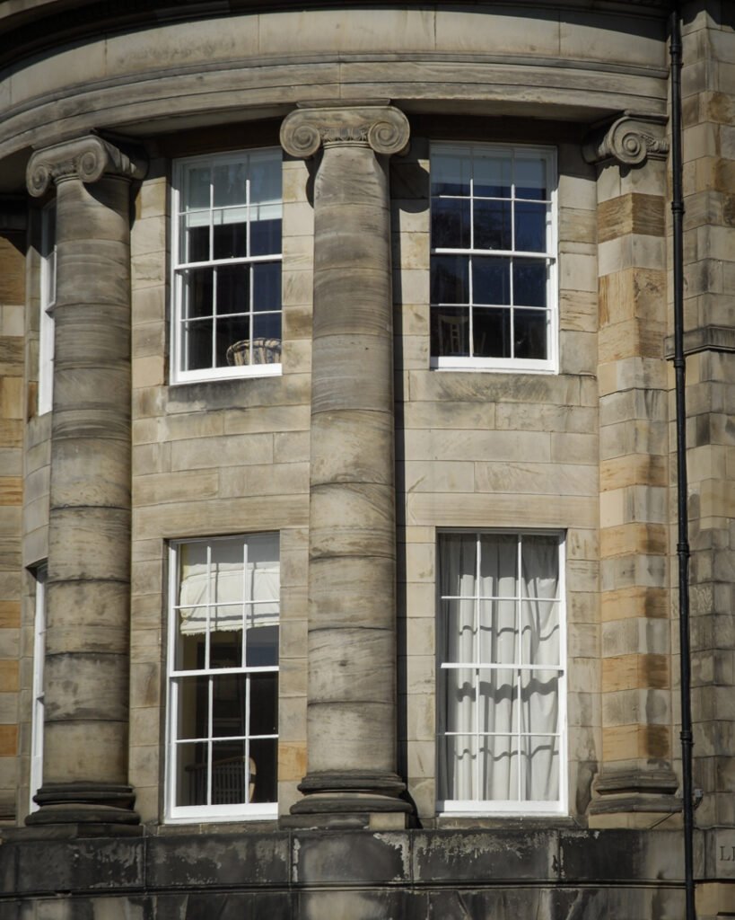 Exterior shot of sash and case windows in a period building with stone columns.