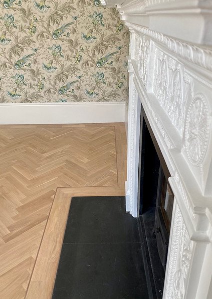 Close-up of herringbone wood flooring around a fireplace in a period home, highlighting detail and craftsmanship.